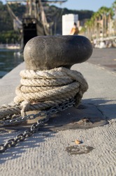 Selective focus of a Old rope And a Chain tied tight in a nautical bollard in the harbour With a blurry background with the boardwalk 