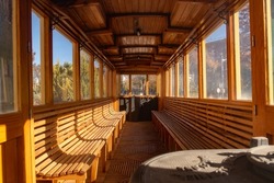 interior of an old tram car in the city of Linares in Spain, with wooden seats and ceiling, and large windows. In the background is a driving position, in the foreground an old steel steering wheel