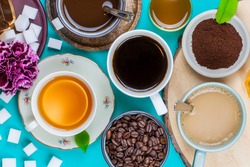 Collection of tea and coffee cups, with sugar cubes and coffee beans, on a pastel blue background. Flat lay, top view.