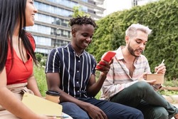 Diverse people having fun eating takeaway food outdoor in the city - Focus on non-binary man