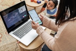 Trader mother studying stock market on streaming lesson with her child at home - Blockchain analysis concept - Focus on left hand holding mobile phone