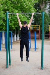 A male athlete is engaged in a horizontal bar, on a sports ground