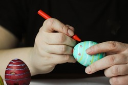 Coloring Easter eggs with pastel red wax crayon. Green Easter egg in women's hands before dyeing colors at home. Easter egg festival. Artistic work, handmade, DIY. People preparing for Easter in April