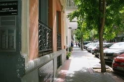 Madrid, Spain. June 1, 2022 Cozy city street stretching into the distance in sunny summer day. Sidewalk with cars parked at a curb, green trees, ancient architecture. Urban scene. Traveling in Europe.