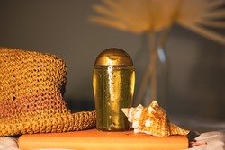 Still life cosmetics composition. Summer body care oil with SPF protection - sunscreen oil in clear bottle with golden liquid. Tanning product. Straw hat, seashell for a holiday at summer seaside