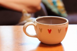 A beautiful pretty white ceramic or clay handmade cup with a picture of hearts. A warm fall winter drink in a mug on the table. A concept of love, harmony, warmth. Romantic mood, dating, love concept.
