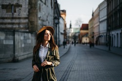 Outdoor fashion portrait of elegant, luxury woman wearing beige hat, sunglasses, trendy white shirt, in a green trench coat, walking in street. Copy, empty space for text. High quality photo