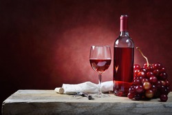 Bottle and glass of rose wine with bunch of grapes on an old wooden table. Space for text.