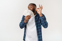 Portrait of young smiling dark skin african american man in white t shirt holding money and showing okay sign isolated on gray background