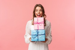 Holidays, celebration and women concept. Portrait of happy cheerful girl likes celebrating birthday and receive presents, holding two gift boxes and smiling camera, pink background