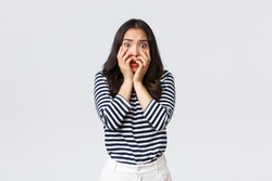Lifestyle, people emotions and casual concept. Scared timid and insecure woman hold hands near mouth, screaming and looking terrified, shivering from fear, stand white background