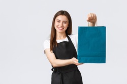 Grocery store employees, small business and coffee shops concept. Friendly helpful, smiling saleswoman handing over customer their bag with purchase, clerk or cashier processing order