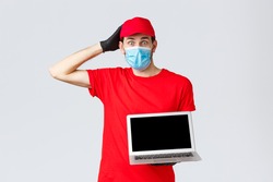 Customer support, covid-19 delivery packages, online orders processing concept. Confused and worried courier in red uniform, face mask and gloves, look nervous, show laptop screen