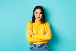 Attractive asian woman with short dark hair, cross arms on chest and smiling confident, standing over blue background