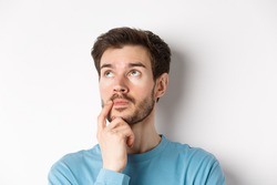 Face of young caucasian man looking up pensive, making choice or thinking, pondering while standing over white background