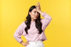 People emotions, lifestyle and fashion concept. Bothered and annoyed asian woman slap forehead and roll eyes displeased, remember something, standing upset yellow background