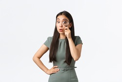Small business owners, women entrepreneurs concept. Surprised funny asian woman searching for something, found product, looking through magnifying glass amazed and impressed