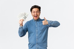 Excited smiling asian man with braces and glasses, showing thumbs-up and waving money, receive paycheck, freelancer got job with good payment, holding cash and looking satisfied