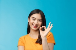 Close-up cute asian friendly girl supports your fantastic idea, smiling broadly, show okay ok sign approval, accept terms, agree take part event, stand blue background satisfied, judging nice work
