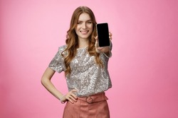 Studio shot confident charismatic young glamour woman introduce awesome smartphone app showing mobile phone display smiling self-assured recommend follow blogger page, standing pink background