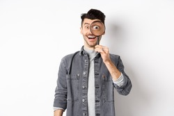 Happy funny guy look through magnifying glass with big eye, checking out interesting deal, searching something, standing on white background