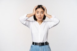 Image of shocked anxious asian woman in panic, holding hands on head and worrying, standing frustrated and scared against white background
