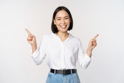 Image of beautiful asian woman pointing fingers left and right, making decision, showing two variants choices, standing over white background
