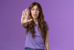 Worried shocked curly-haired woman gasping stare camera anxiously pull hand stop sign begging end prohibiting friend drive after drinking stand purple background forbid warn you purple background
