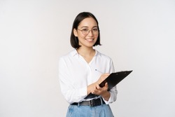 Image of smiling korean office lady, company employee writing down on clipboard, taking notes, standing over white background