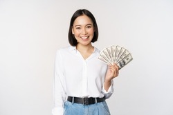 Credit and loan concept. Smiling young asian woman holding cash dollars and looking happy at camera, white background