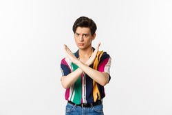 Disappointed young queer man telling no, showing stop gesture and forbid something bad, standing over white background