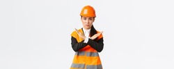 Serious-looking fed up asian female boss, construction manager in safety helmet showing cross gesture to stop, prohibit dangerous action, disappointed with result, forbid something