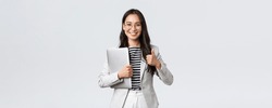 Business, finance and employment, female successful entrepreneurs concept. Confident good-looking therapist or businesswoman in white suit, holding laptop and showing thumbs-up