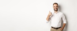 Satisfied successful boss showing thumb up, approve and praise good work, standing over white background.