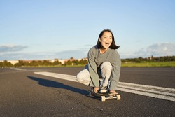 Freedom and happiness. Happy asian girl riding her longboard on an empty sunny road, laughing and smiling, skateboarding.