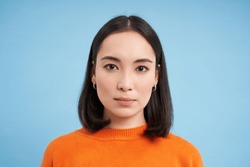 Close up of candid young asian woman, looking at camera with genuine, natural emotions, standing over blue background.