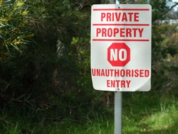 A well worn and bent Private Property No unauthorized entry sign with a green bushy backdrop. 
