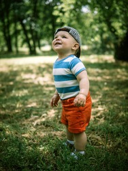 Cute little baby boy walks through the summer park. Child is laughing. Adorable baby boy in a baseball cap. Baby boy runs on the green grass for soap bubbles.  Happy child in the forest.