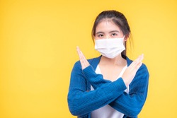 Asian girl wearing Face Mask show stop hands gesture for stop corona virus Covid19outbreak on yellow background , protect spread Covid-19