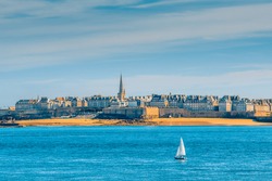 Saint-Malo, Brittany, France: Panoramic view of the walled old town, Intra-Muros, with a solitary sailing boat in the foreground from Dinard, a popular and prestigious seaside resort nearby. 