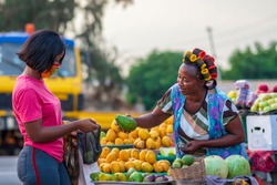 A young African buying fruits from the market and wearing face mask for protection - Receiving a purchased item from a local happy food vendor - Black millennial lifestyle in covid-19 pandemic season.