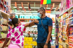 Two young Africans wearing face mask for protection,shopping in a supermarket, greeting each other with elbow, practicing social distancing - Black millennial healthy lifestyle in covid-19 pandemic