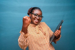 Portrait of a beautiful woman wearing spectacles,holding a file and feeling successful,winning,celebrating isolated on a blue studio background