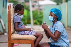 portrait of African health worker wearing surgical face mask and attending to a child patient also wearing a homemade mask for protection in covid-19 pandemic season-concept on child healthcare