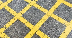 No parking area sign on the asphaltic surface, Yellow crossing sign on the textured floor, Yellow logo on grey color background
