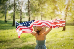 Closeup back view of a Proud woman enjoying summer sunset outdoors and holding american flag