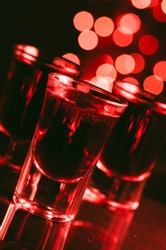 Red alcohol cocktails in shot glasses over red bokeh light  background. Shots on bar counter in night club party.