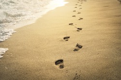 Footprints in the sand at sunset. Beautiful sandy tropical beach with sea waves. Footsteps on the shore.