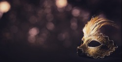 Golden venetian ball mask in front of the night bokeh lights. Masquerade party or holiday event celebration concept. 