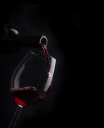 Red wine pouring in wineglass from bottle over black background. Wine list design menu with copyspace. Alcohol beverage card backdrop.